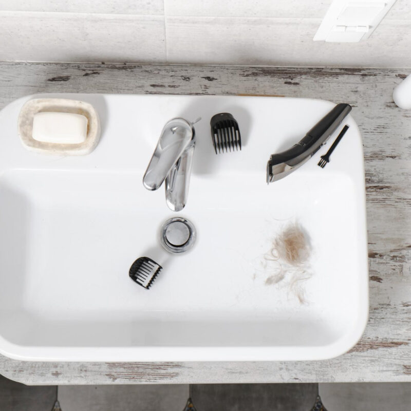Bathroom sink with shaving instruments and some pubes after man has shaved in prep for his vasectomy