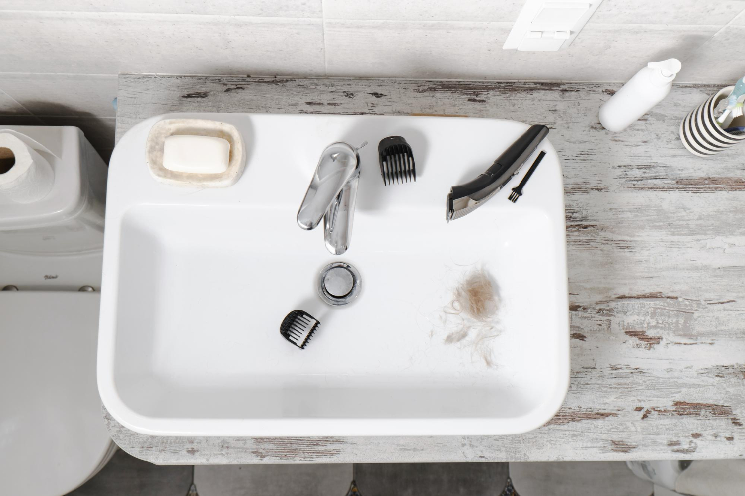 Bathroom sink with shaving instruments and some pubes after man has shaved in prep for his vasectomy